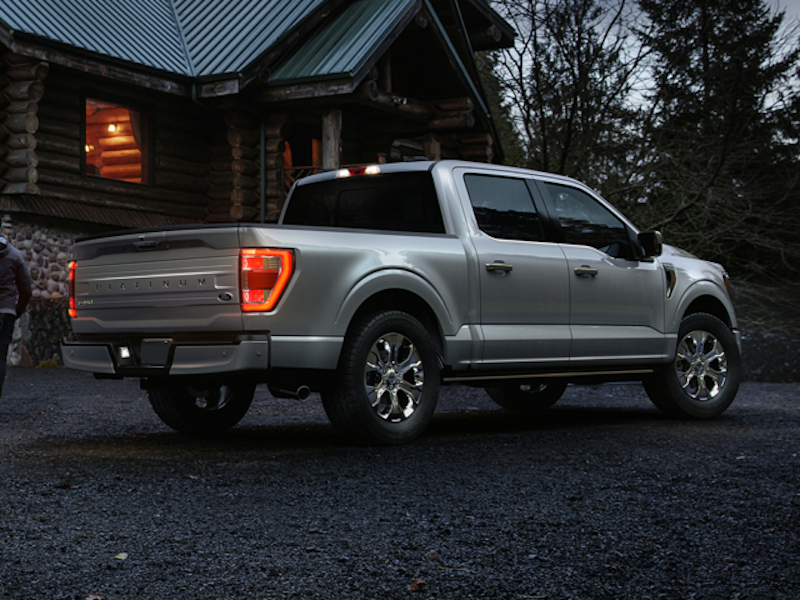 A picture of the 2024 Ford F-150 from behind, parked in front of a log cabin